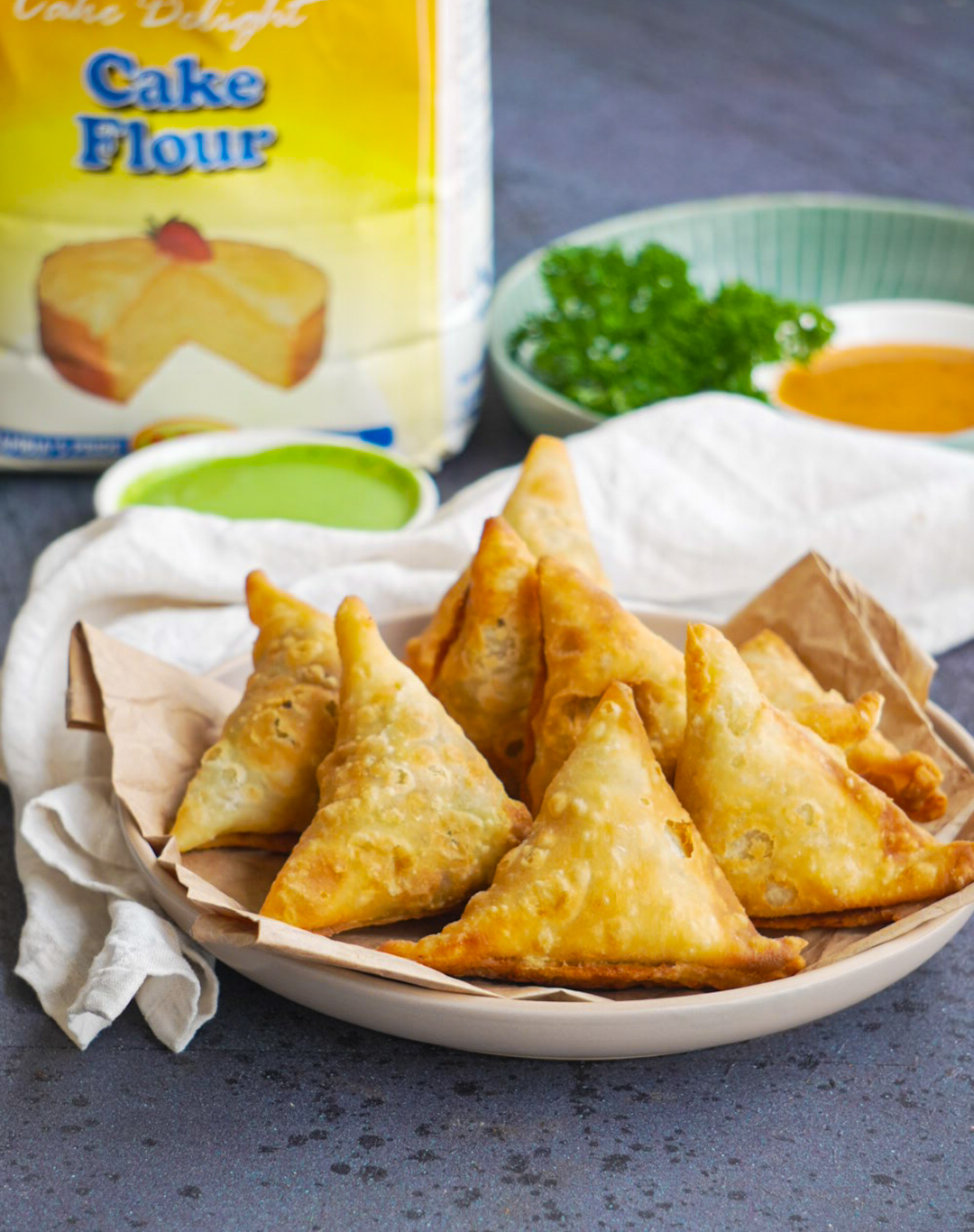 Golden fried samosas styled with Cake Delight cake flour packaging and dipping sauces