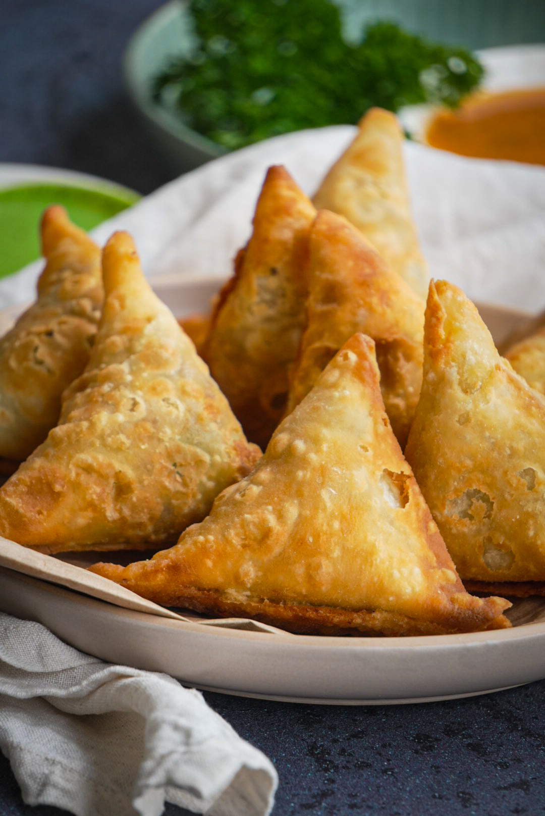 Golden fried samosas plated with fresh coriander and dipping sauces